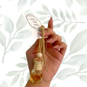 May include: A small, clear glass aromatherapy bottle filled with amber liquid, suspended by a gold cord and wooden bead. The bottle has a wooden cap and is attached to a white tag with the text "Coffee Shop".