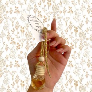 May include: A small, clear glass aromatherapy bottle filled with a golden liquid, suspended by a gold cord and wooden bead. The bottle is labeled "Coffee Shop Aromatherapy". The background features a floral pattern.