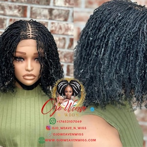 Puede incluir: Peluca negra con micro trenzas, peinada en un corte bob corto y rizado. La peluca se muestra en una cabeza de maniquí, mostrando el intrincado patrón de trenzado y la línea de cabello de aspecto natural. Fondo con pared de ladrillos y top verde.