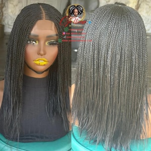 Könnte beinhalten: Eine schwarze geflochtene Perücke mit Mittelscheitel, präsentiert auf einer Schaufensterpuppe. Die Perücke hat lange, dünne Zöpfe und einen natürlich aussehenden Haaransatz. Die Schaufensterpuppe hat gelben Lippenstift und ein schwarzes Oberteil. Die Perücke wird von vorne und hinten gezeigt.