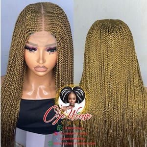 Könnte beinhalten: Eine lange, goldbraune geflochtene Perücke mit Spitzenfront. Die Perücke hat einen Mittelscheitel und ist mit zahlreichen kleinen Zöpfen versehen. Das Bild enthält ein Logo mit dem Text "Ojo Weave".