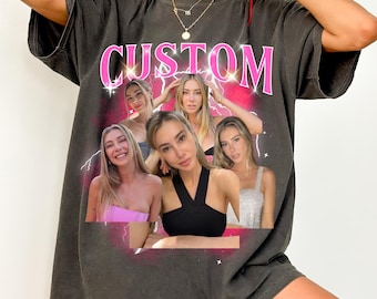 May include: Dark gray t-shirt with a pink and white graphic. The graphic features the word "CUSTOM" above a collage of six women. The shirt has short sleeves and a relaxed fit.