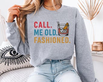 Puede incluir: Una sudadera gris jaspeado con el texto "CALL. ME OLD. FASHIONED." en rojo, azul y amarillo. Un gráfico de un cóctel Old Fashioned está a la derecha del texto. La sudadera es de estilo casual.