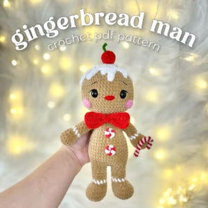 May include: A crocheted gingerbread man doll with a red bow tie, candy buttons, and a candy cane. The doll has white icing details, a red cherry on top, and the text "gingerbread man crochet pdf pattern".