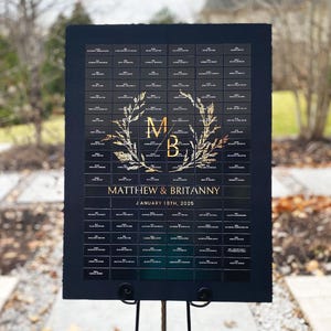 Könnte beinhalten: Schwarze Hochzeitssitzordnung mit goldenen Buchstaben und einem floralen Design. Die Karte listet die Namen der Gäste und ihre zugewiesenen Tische auf. Der Text lautet "Matthew & Brittany" und "January 18th, 2020".