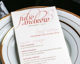 May include: A white wedding menu card with gold lettering. The menu includes a strawberry and jicama salad, filet mignon, Asian salmon, autumn tartlet, double baked potato, and wedding cake.
