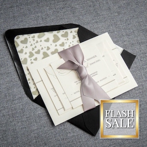 May include: A set of wedding invitations with a black envelope, a white card with a gray ribbon, and a white card with a pattern of gray hearts. The text on the card reads "Dinner and Dancing".