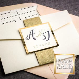 May include: A wedding invitation with a gold glitter background and a white square with the text "A and J 11.14.16" in black lettering.