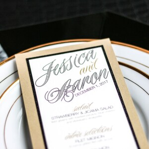 May include: A tan card with black trim and a white background. The text "Jessica and Baron" is written in a cursive font with a silver glitter effect. The date "December 1, 2017" is written in a smaller font below the names. The card lists a "salad" option with the text "Strawberry & Jicama Salad".