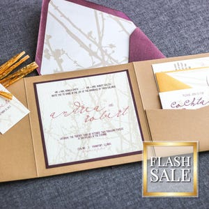 Op de afbeelding: Een bruine uitnodigingsenvelop met een bordeauxkleurige flap. De envelop heeft een zakje aan de binnenkant dat een kleinere witte envelop met een gouden rand bevat. De witte envelop heeft de tekst "Cocktails" erop gedrukt. De uitnodiging is voor een bruiloft en heeft de namen "Andrea en Robert" erop gedrukt.