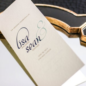 Puede incluir: Una invitación de boda con fondo crema y texto azul marino. La invitación dice "The Wedding Celebration of Lisa Williams & Sean Stather June 18, 2016 Chicago, Illinois"