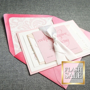 Può includere: Set di inviti di nozze rosa e bianco con un nastro di raso bianco. L'invito include il testo "Cocktail Hour" e "Dinner and Dancing".
