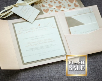 May include: A blush pink wedding invitation with a white inner envelope and a tag that says "Giana and Joel,  Announcing our Engagement". The invitation is decorated with a delicate pattern of hearts.