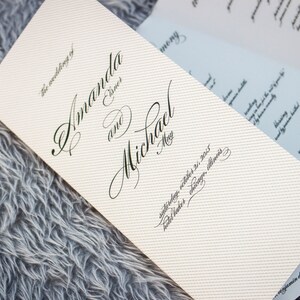 May include: A white wedding programme with black calligraphy announcing the wedding of Amanda and Michael. The date is Saturday, 24th October 2015, with the location listed as Chicago, Illinois.