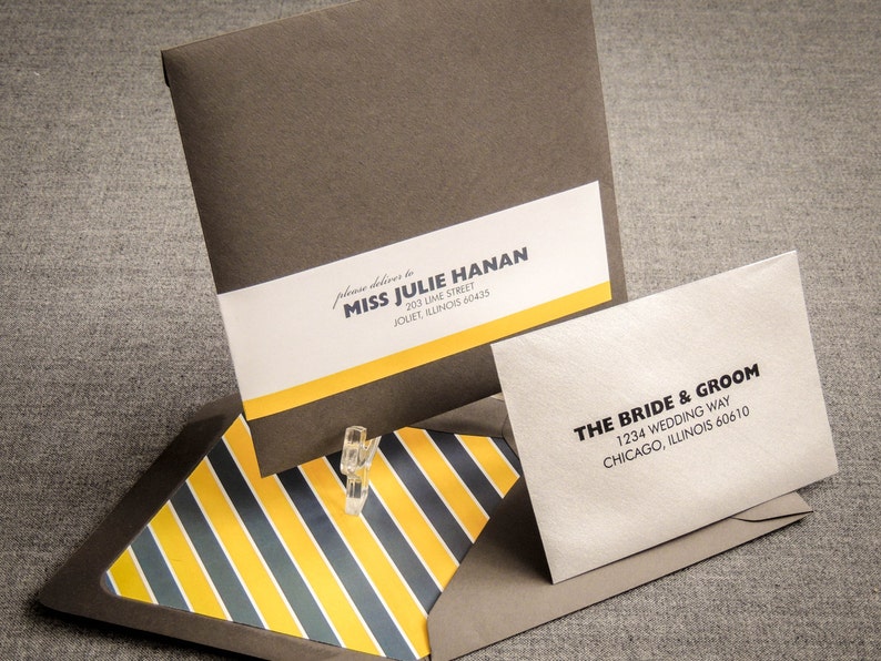 May include: A brown envelope with a yellow and black striped envelope flap. The envelope has a white label with the text "please deliver to Miss Julie Hanan, 203 Lime Street, Jouet, Illinois 60435". A smaller white envelope with the text "The Bride & Groom, 1234 Wedding Way, Chicago, Illinois 60610" is on top of the envelope.