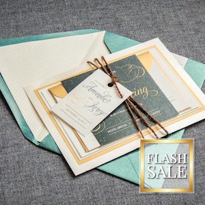 May include: A wedding invitation suite with a teal envelope, a cream card with gold trim, and a dark blue card with gold lettering. The text on the card reads "Amanda and Jerry, September 10, 2017, at six o'clock, Hotel Arista".