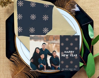 Può includere: Un biglietto di auguri natalizio con una foto di una famiglia di quattro persone davanti a un paesaggio innevato. Il biglietto ha uno sfondo blu scuro con un motivo di fiocchi di neve rosa e il testo "Buon Anno Nuovo" in lettere dorate. Il testo "The Patel Family - 2021" è in fondo al biglietto.