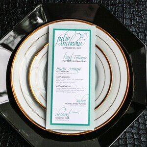 Puede incluir: Una tarjeta de menú de boda con un borde turquesa y detalles dorados. El menú incluye el primer plato, el plato principal, los acompañamientos y el postre. El texto en la tarjeta dice "Julie Andrew, 23 de septiembre de 2017, Primer plato: Ensalada de fresa y jicama, Plato principal: Filete mignon, Salmón asiático, Tarteleta de otoño, Acompañamientos: Papa doble horneada, Postre: Pastel de boda."