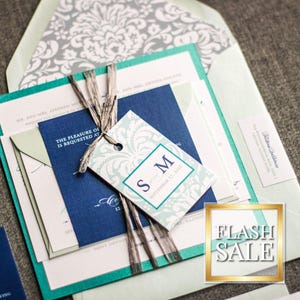 May include: A teal, blue, and white wedding invitation suite with a decorative tag that says "S.M." and a white damask pattern. The invitation is on a light green background.