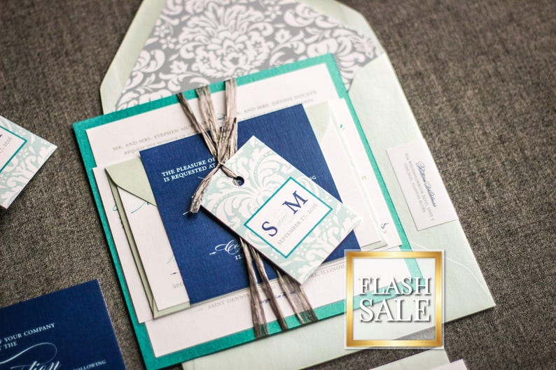 May include: A teal, blue, and white wedding invitation suite with a decorative tag that says "S.M." and a white damask pattern. The invitation is on a light green background.