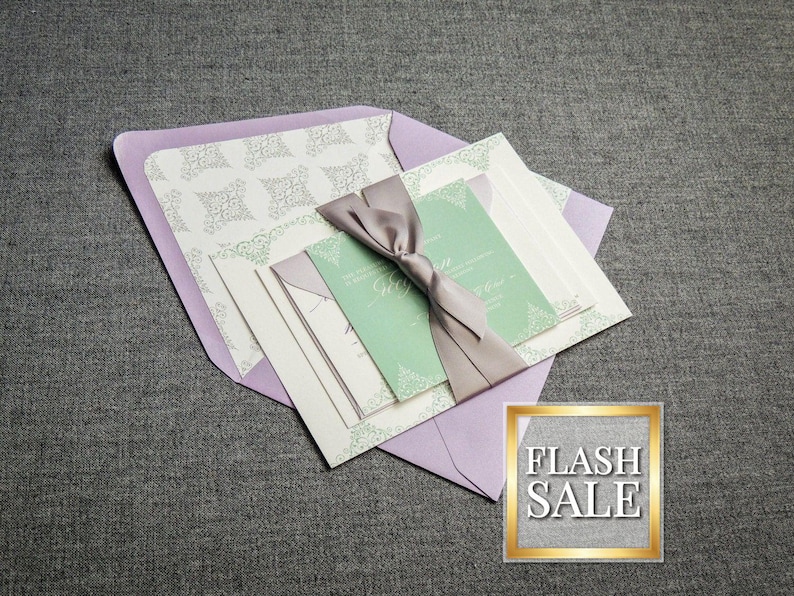 May include: A set of wedding invitations with a lavender envelope, white cardstock, and a green inner card. The cards are tied together with a gray satin ribbon.