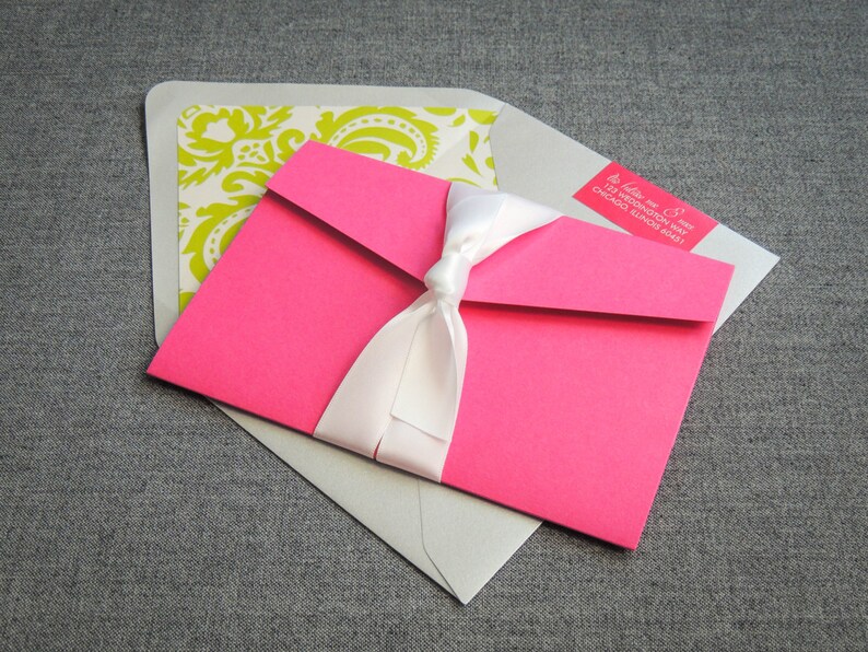 Pode incluir: Um envelope rosa com uma fita branca e um envelope branco com um padr&atilde;o verde e branco. O envelope rosa tem um r&oacute;tulo de endere&ccedil;o de retorno com o texto "Julie & Mike 123 Weddington Way Chicago, Illinois 60641".