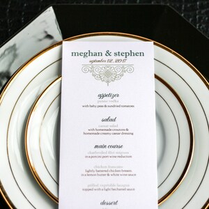 May include: A wedding menu card with gold trim and a decorative design. The menu includes appetizers, salad, main course, and dessert. The text on the card reads "meghan & stephen" and "september 12, 2017".