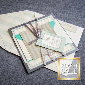 May include: A wedding invitation suite with a striped envelope, a gray and white striped card with the text "Cocktail Dinner", a light blue card with the text "Amanda & Jason", and a white card with the text "Save the Date".