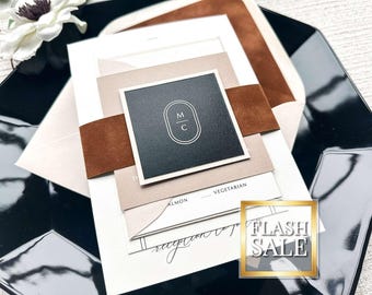 May include: An elegant wedding invitation suite featuring a black square card with white initials, a brown suede band, and layered neutral-toned cards. The suite is displayed on a black, glossy surface. The words "Vegetarian" and "Reception" are visible. A "Flash Sale" graphic is in the corner.