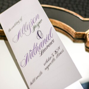 May include: A white wedding programme with the names "Allison Jasper & Nathaniel Lawrence" in purple calligraphy. The date "October 5, 2017" and the location "Hotel Arista Naperville, Illinois" are printed in black.