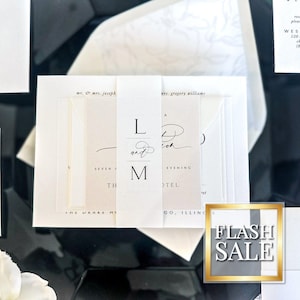 Puede incluir: Un conjunto de invitaciones de boda blancas con un diseño sencillo. La invitación presenta las iniciales de la pareja "L" y "M" en una fuente minimalista. El texto "Seven O'Clock in the Evening" está impreso en la invitación. La invitación está doblada por la mitad y tiene una superposición de plástico transparente.