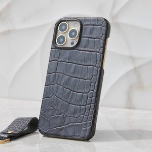 May include: A black leather phone case with a crocodile pattern and gold accents. The case is designed for an iPhone and has a matching key chain.
