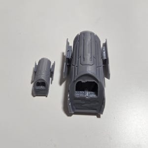 Peut inclure: Deux objets cylindriques gris avec des motifs complexes et nervurés. L'un est plus grand, avec un intérieur creux, et l'autre est une version plus petite. Les deux ont des panneaux latéraux attachés, suggérant un thème mécanique ou architectural.