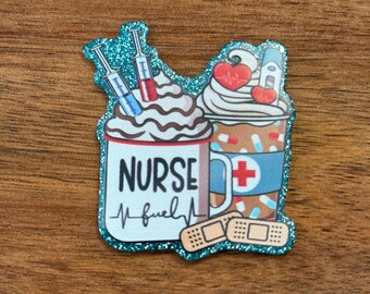 May include: A teal glittery badge featuring two coffee mugs with whipped cream and medical-themed designs. One mug says "NURSE fuel" with a heartbeat line, and the other has a red cross and a thermometer. Syringes and bandages are also included.