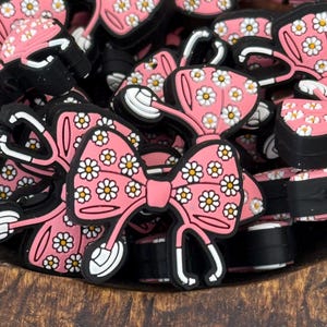 May include: A bowl filled with pink and white bow charms with a daisy print. The charms have a black stethoscope design.