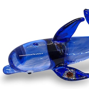 May include: A handcrafted glass dolphin figurine in a vibrant cobalt blue hue. The sculpture features translucent glass with swirling white patterns, a dark band near the head, and shimmering copper-coloured glitter accents on the fins and tail.