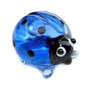 May include: A blue glass ladybug figurine with black spots and a black head. The ladybug has clear glass legs and antennae. The figurine is a decorative item.