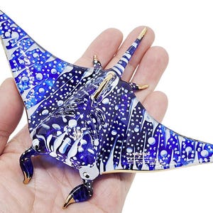 May include: A blue and white glass sculpture of a manta ray with gold accents. The sculpture is detailed with white spots and a blue and white patterned design.