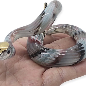 May include: A glass snake ornament with a gold head and a body of swirling grey, white, and maroon colours. The snake is coiled and appears to be resting on a hand.