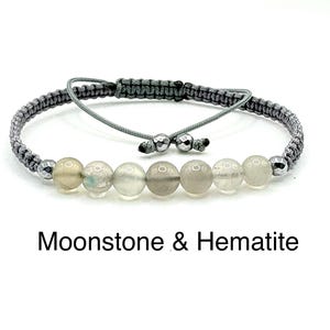 May include: A grey macrame bracelet with six translucent moonstone beads and two silver beads. The bracelet is adjustable with a sliding knot. The text "Moonstone & Hematite" is below the bracelet.