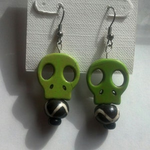 Light green skull sitting on a black and white bead dangle wire earring.