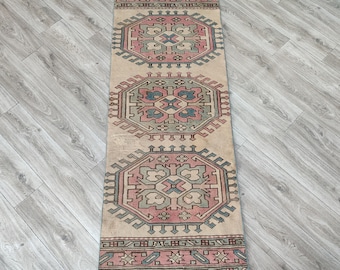 May include: A rectangular, vintage-style rug with a beige background and geometric patterns in pink, blue, and green. The rug features repeating octagonal designs and a detailed border, suitable for a hallway or entryway.