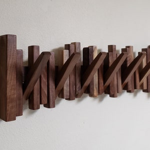 May include: A wall-mounted wooden coat rack with multiple hooks. The rack is made of dark brown wood and has a modern design.