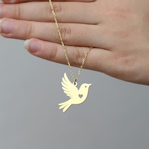 Puede incluir: Un collar de oro con un colgante de paloma. La paloma tiene un coraz&oacute;n cortado en su pecho.