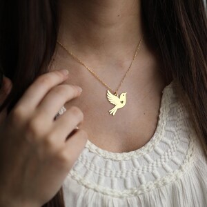 Puede incluir: Un collar de oro con un delicado colgante de paloma con un peque&ntilde;o coraz&oacute;n recortado. La paloma es un s&iacute;mbolo de paz y amor.