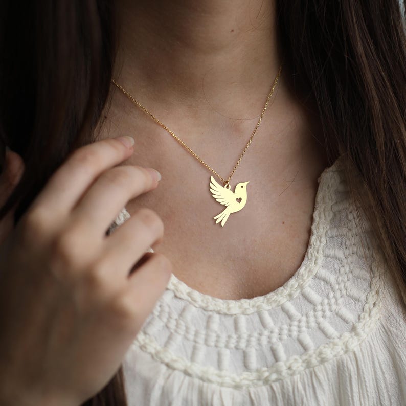 Puede incluir: Un collar de oro con un delicado colgante de paloma con un peque&ntilde;o coraz&oacute;n recortado. La paloma es un s&iacute;mbolo de paz y amor.