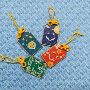 May include: Four rectangular wooden charms with yellow cord loops. One is teal with a tiger, one is dark blue with a wolf and moon, one is red with a fox and flowers, and one is green with a bear and leaves. Each charm features a unique animal illustration.