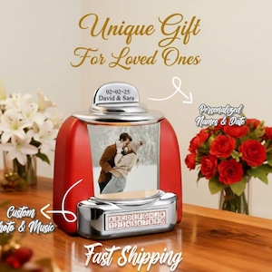 Op de afbeelding: Een rode en zilveren muziekspeler in jukebox-stijl met een foto van een stel. De tekst op de jukebox luidt "Unique Gift For Loved Ones", "Custom Photo & Music" en "Personalized Names & Date". De datum "02-02-25" en de namen "David & Sara" worden ook weergegeven.