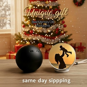 May include: A black spherical speaker and a round photo display with a silhouette of a mother and child are on a wooden surface. The photo display is lit from within. The text reads "Unique gift" and "Best Memory Orb For Mom's".