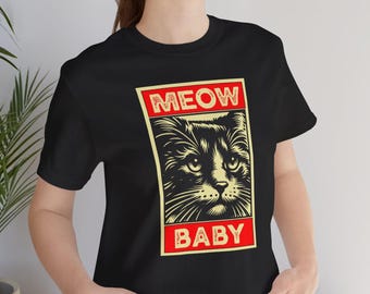 May include: Black t-shirt with a cat graphic and the text "MEOW BABY" in a red frame. The cat's face is detailed with whiskers and expressive eyes, set against a cream background.